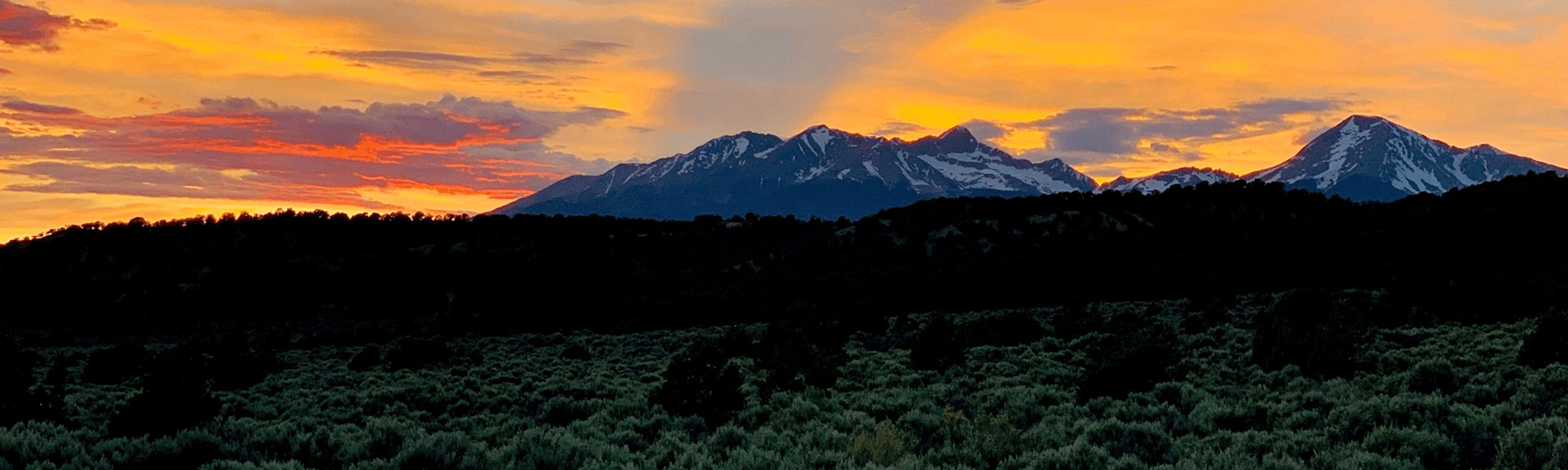 Sunset over snow-capped Mt. Blanca Massif with silhouetted hills and piñon pines in the Sangre de Cristo Ranches, Southern Colorado